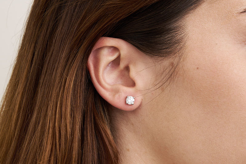 Close-up of an ear wearing a diamond earring with a neutral background