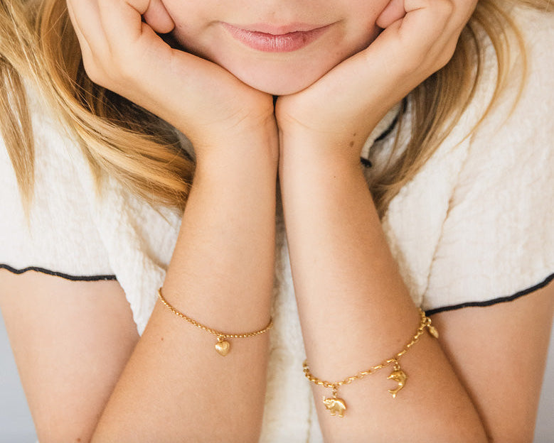 Child wearing gold bracelets with charms on a plain background, labeled 'Children's Jewellery'.