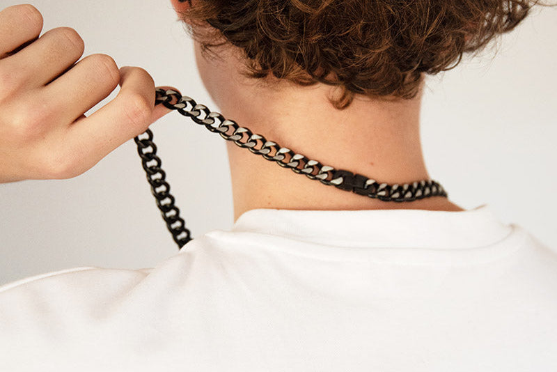 Person adjusting a chain necklace on a plain background