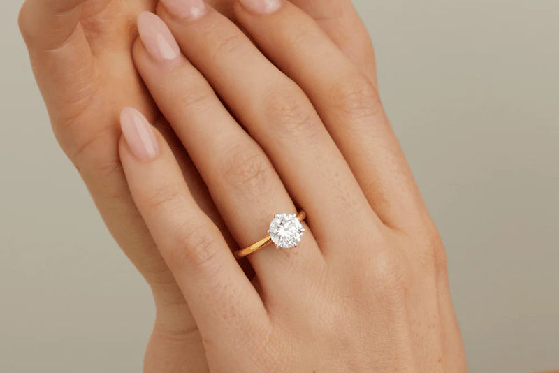 Gold ring with a diamond on a hand against a neutral background