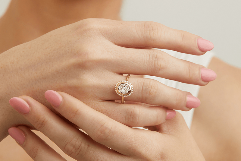 Rose gold ring with a diamond on a hand with pink nail polish.