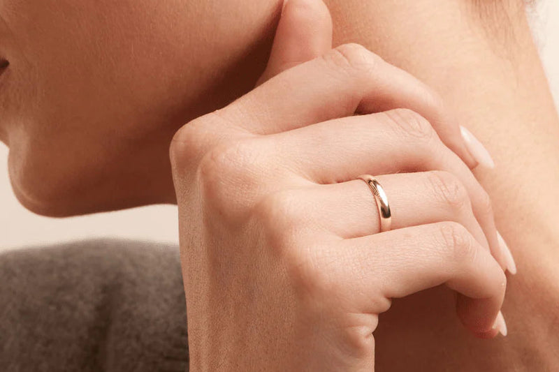 Close-up of a hand wearing a gold ring on a neutral background