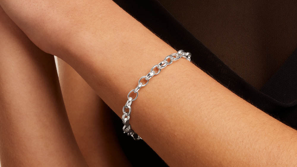 A close-up of a person's wrist wearing a polished silver chain bracelet, paired with a black top.