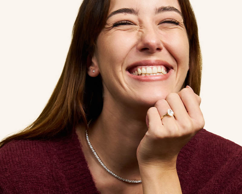 Woman wearing a diamond ring and bracelet, smiling with hand on chin against a plain background