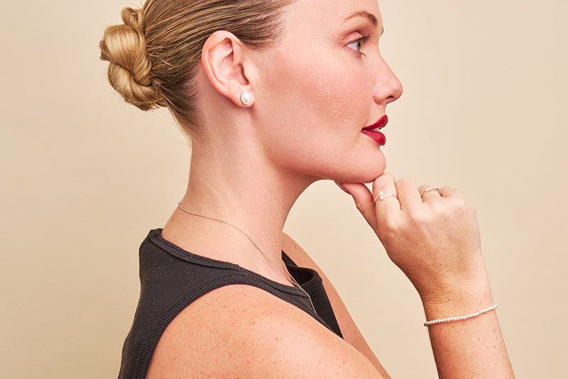 Woman with styled hair and jewelry against a beige background